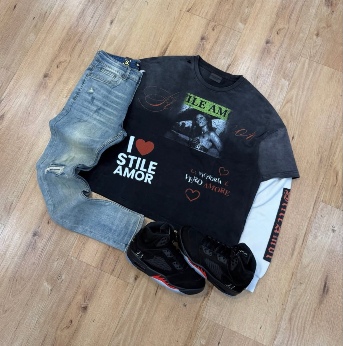 Photograph of complete streetwear outfit: faded black graphic top, white long sleeve, distressed denim jeans and black red sneakers